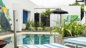 Un espace piscine avec des chaises longues, une fresque murale et un parasol noir.