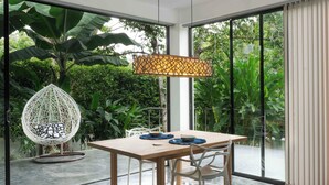 Un espace repas moderne avec une table en bois, des chaises blanches et un fauteuil suspendu agrémenté d’un coussin à motifs.
