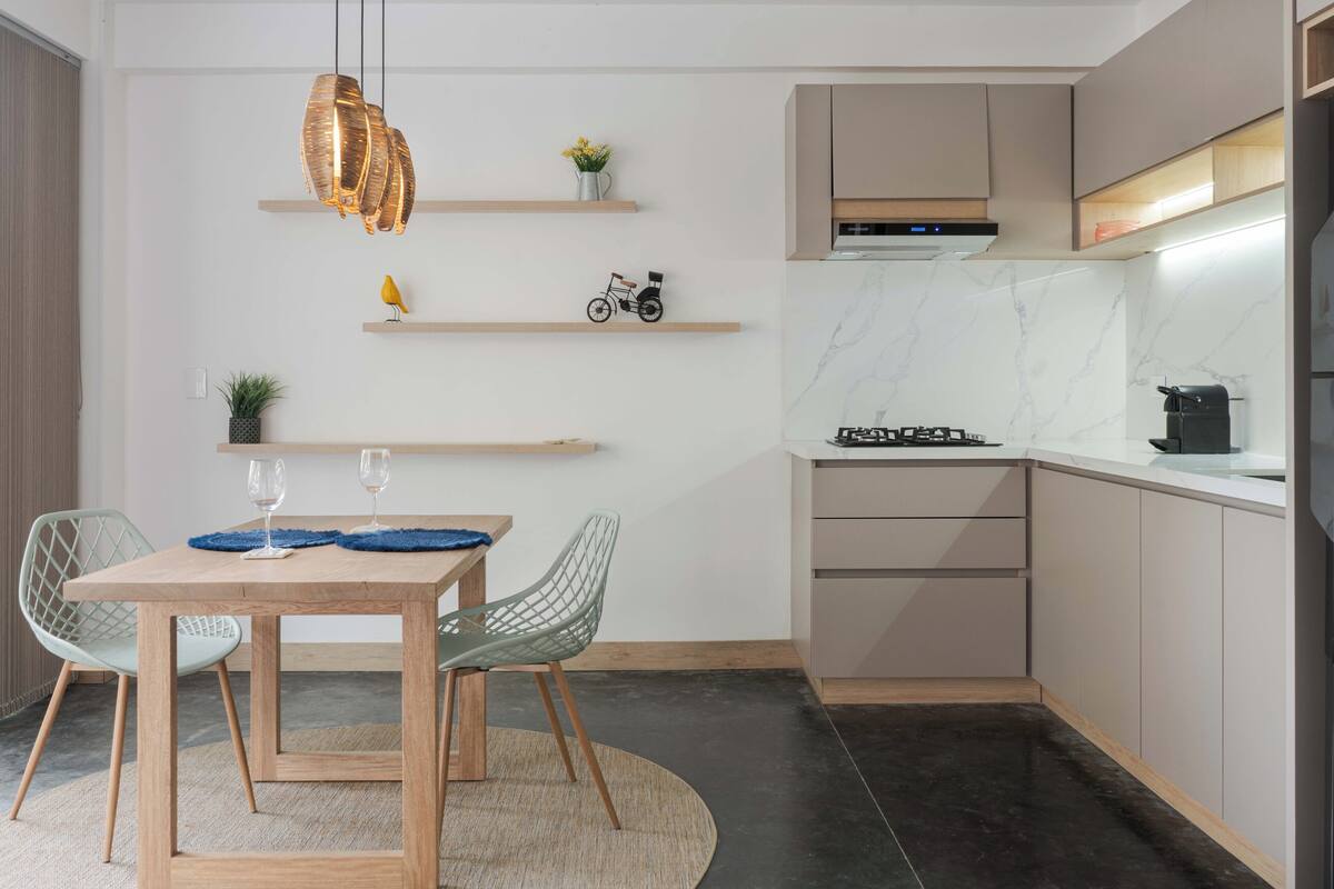 Eine moderne Küche mit Essbereich, ausgestattet mit einem Holztisch, zwei Stühlen, einer Hängelampe und einbaufertigen Schränken.