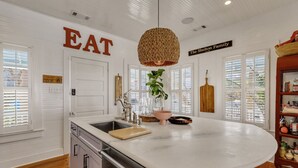 A kitchen with a large island, white cabinetry, and a hanging woven light fixture. - Big Mama`s Beach House! Available limited time only! 5 BDRs, POOL (Tybee Island)