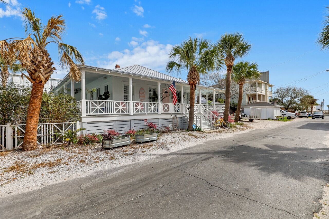 A coastal house with a porch, palm trees, and a clear sky.