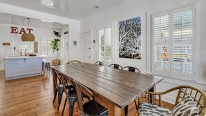 A spacious dining area with a wooden table and chairs, a kitchen island, and large windows with blinds. - Big Mama`s Beach House! Available limited time only! 5 BDRs, POOL (Tybee Island)