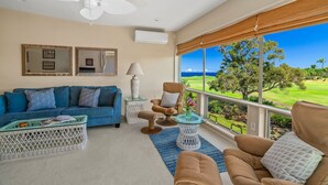 A spacious living room with a blue sofa, beige armchairs, a white coffee table, and a view of a golf course.