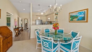 A dining area with a glass table and white chairs, a chandelier, and a painting on the wall.
