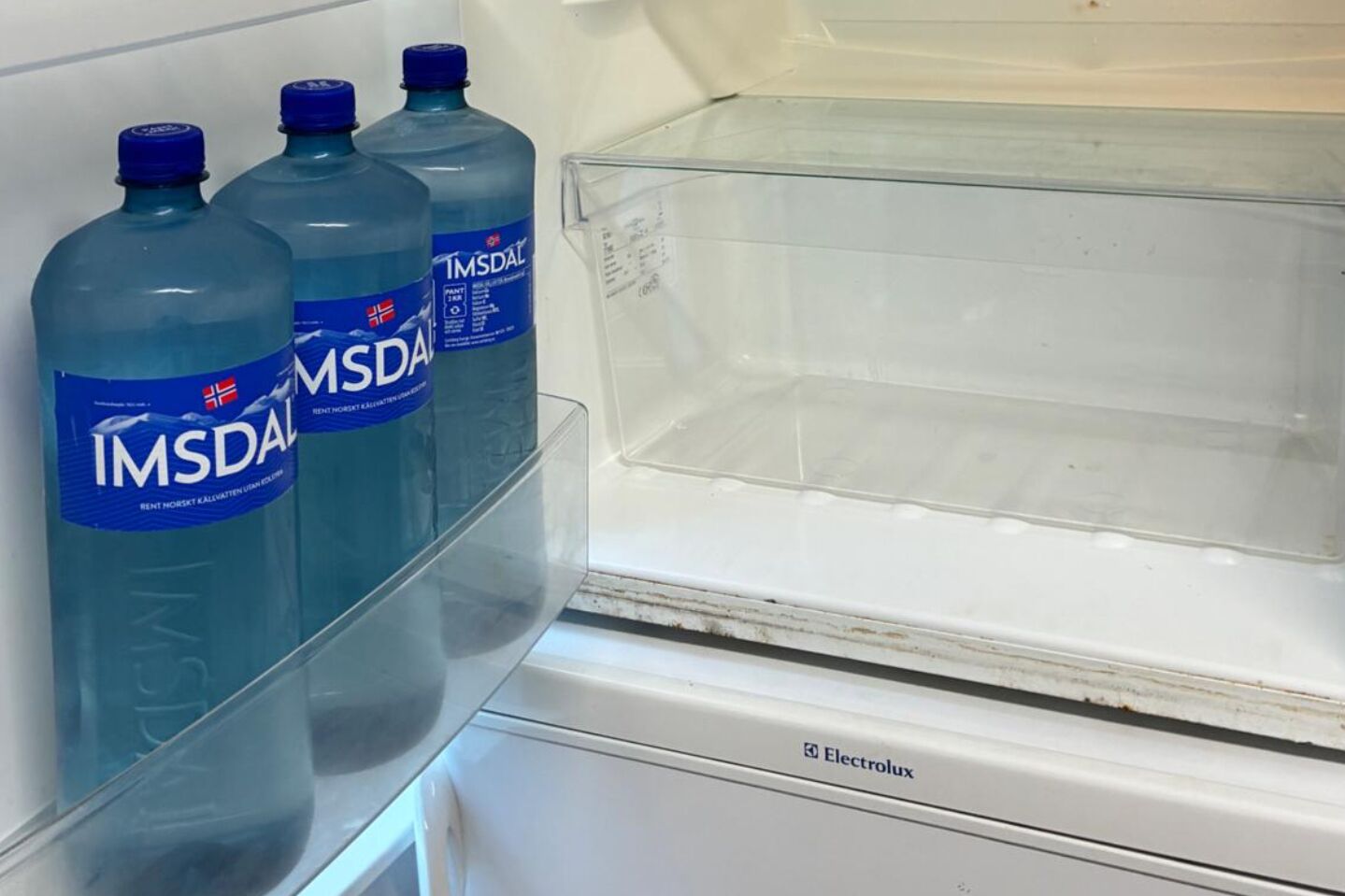 A refrigerator with three IMSDAL water bottles on the door shelf.