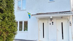 Una casa de fachada blanca, con dos puertas, un ventanal pequeño e izada la bandera sueca.