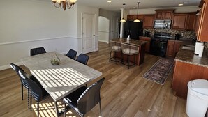 A modern kitchen with wooden cabinets, a central island, and a dining area with a table and chairs. - Spacious 4-bedroom home in private nature (Moore)