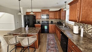 A modern kitchen with granite countertops, wooden cabinets, stainless steel appliances, and a bar area with stools. - Spacious 4-bedroom home in private nature (Moore)