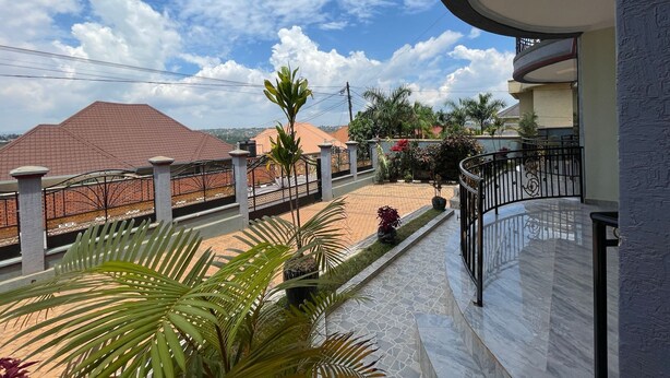 Balcón residencial con vista a casas vecinas, piso de baldosas y plantas en macetas.