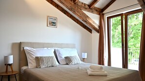 Une chambre avec un grand lit, des poutres en bois, une fenêtre donnant sur un paysage verdoyant et une petite table avec une lampe.