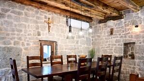 Un coin repas rustique avec un mur en pierre, des poutres en bois au plafond et une table en bois entourée de chaises.