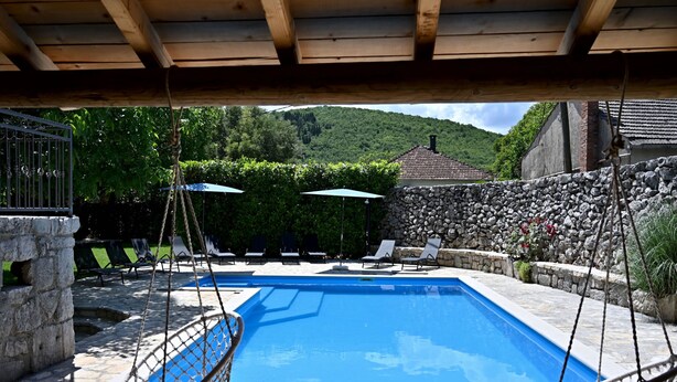 Une piscine dotée d’une terrasse en pierre, entourée de chaises longues et agrémentée d’un fauteuil suspendu.
