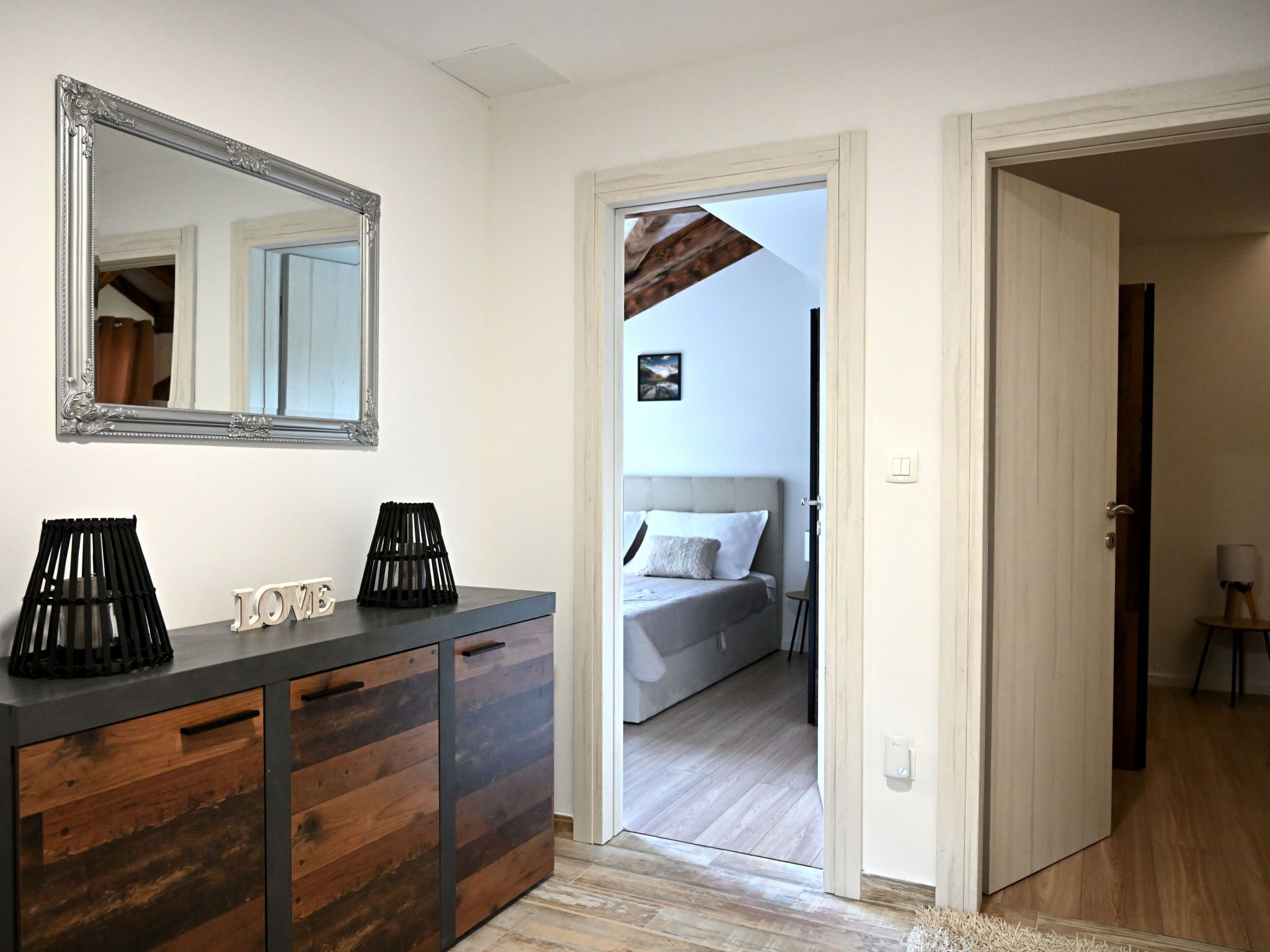 A modern bedroom with a large mirror, a bedside table with a lamp, and a bed with a headboard.