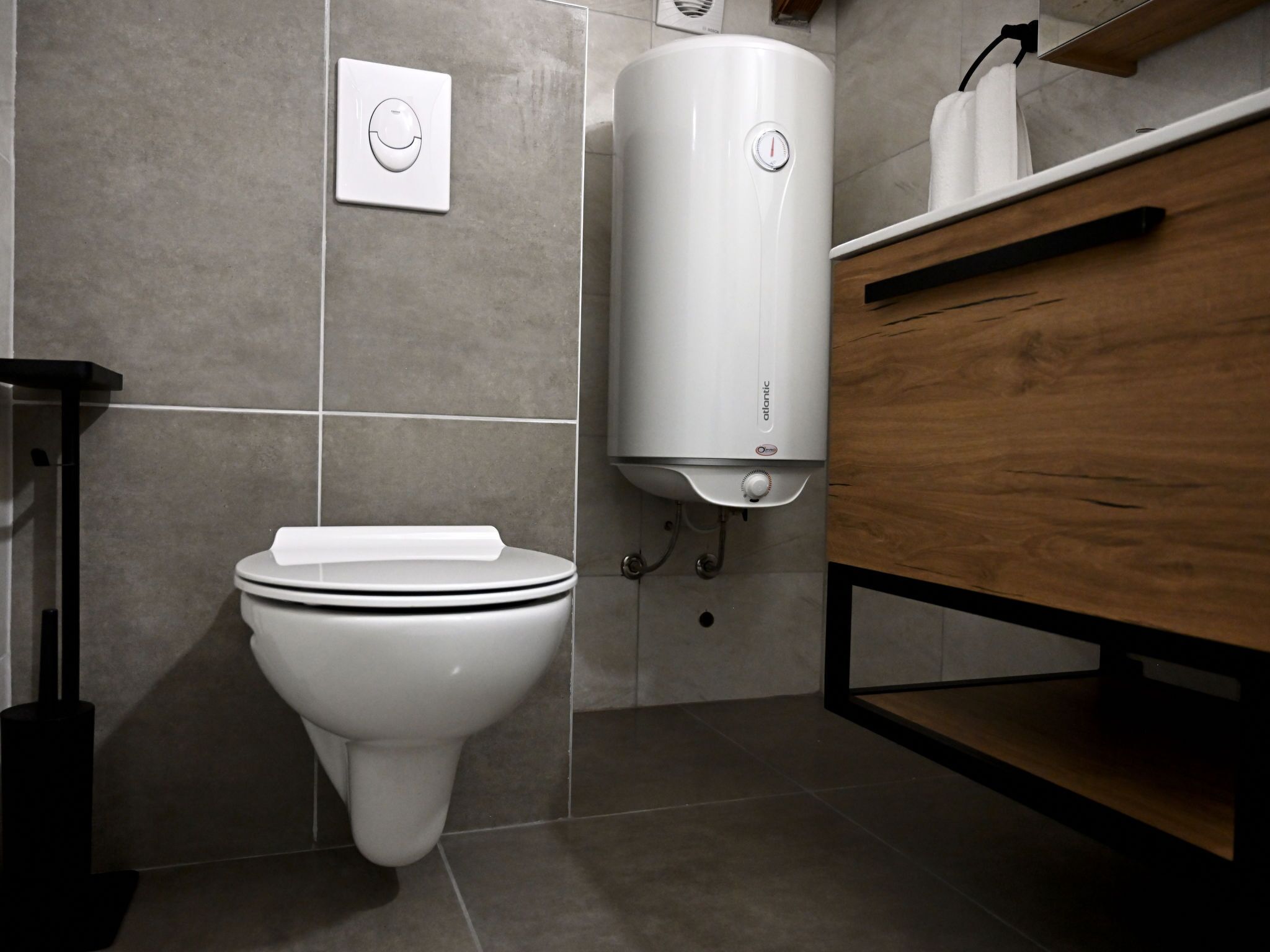 A modern bathroom with a toilet, a wall-mounted water heater, and a wooden vanity.