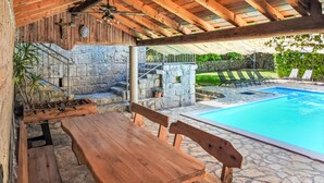Un espace extérieur aménagé avec des sièges en bois, un mur en pierre et une piscine en arrière-plan.