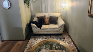Una habitación acogedora con un sofá blanco, un dosel decorativo, una mesa redonda con una bandeja y una araña.