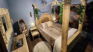 Una cama con dosel y cuatro columnas, un espejo, una mesita de noche con lámpara y una lámpara de pared.