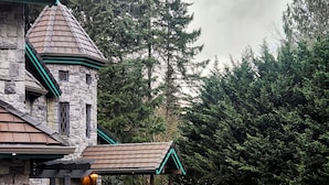 Un edificio de piedra con una torre y un porche cubierto, rodeado de un jardín con varias estatuas y un estanque.