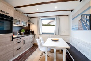 Una cocina moderna con armarios de madera, horno empotrado y comedor con mesa y sillas blancas.