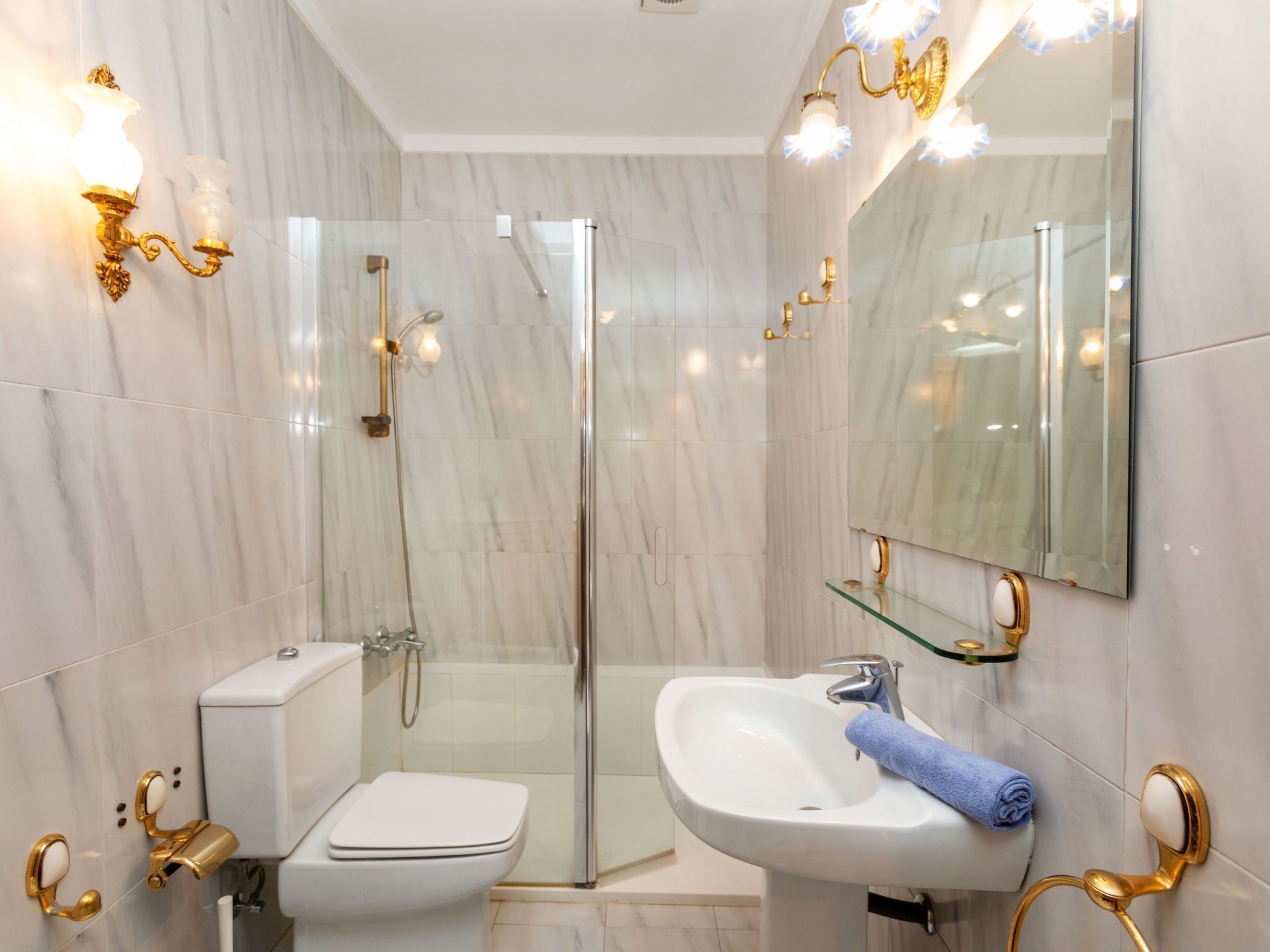 Une salle de bain moderne avec une douche à parois de verre, un lavabo blanc doté de robinetterie dorée et un grand miroir.