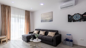 Een moderne woonkamer met een grijze bank, een klein bijzettafeltje en een dartbord aan de muur.