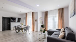 Een moderne woonkamer met een eethoek, een bank en een aan de muur bevestigde televisie.