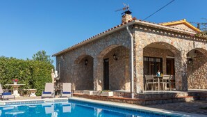 Un bâtiment en pierre doté d’une piscine, caractérisé par une façade en pierre, des fenêtres en arc de cercle et un toit recouvert de tuiles.