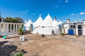 A white building with conical roofs, a blue door, and a small outdoor seating area with a table and chairs.