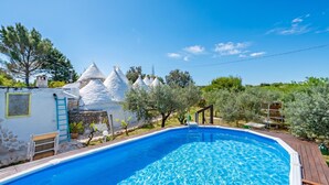 Una piscina amb terrassa de fusta, estructures còniques blanques i oliveres.