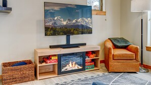 Una sala de estar con un televisor de pantalla plana sobre un soporte de madera, una chimenea, un sillón de cuero y una cesta de mimbre.
