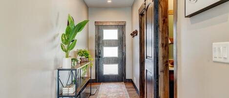A hallway with a wooden door, a potted plant, a metal shelf, and a patterned rug.