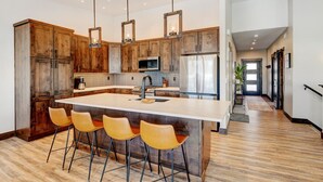 Una cucina moderna con mobili in legno, una grande isola con sgabelli da bar, elettrodomestici in acciaio inossidabile e luci a sospensione.