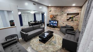 Una sala de estar moderna con un sofá gris, una mesa de centro y un televisor montado en una pared de piedra.