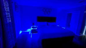 Una habitación con poca luz, con cama, mesita de noche y lámpara de pared.