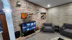 Un salón con pared de piedra, una guitarra colgada, un televisor de pantalla plana y dos sofás grises.