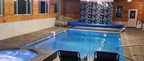 An indoor swimming pool with two chairs, a wooden ceiling, and a patterned wall.