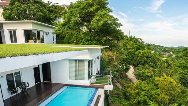 A modern house with a swimming pool, a covered patio, and lush greenery surrounding the property.