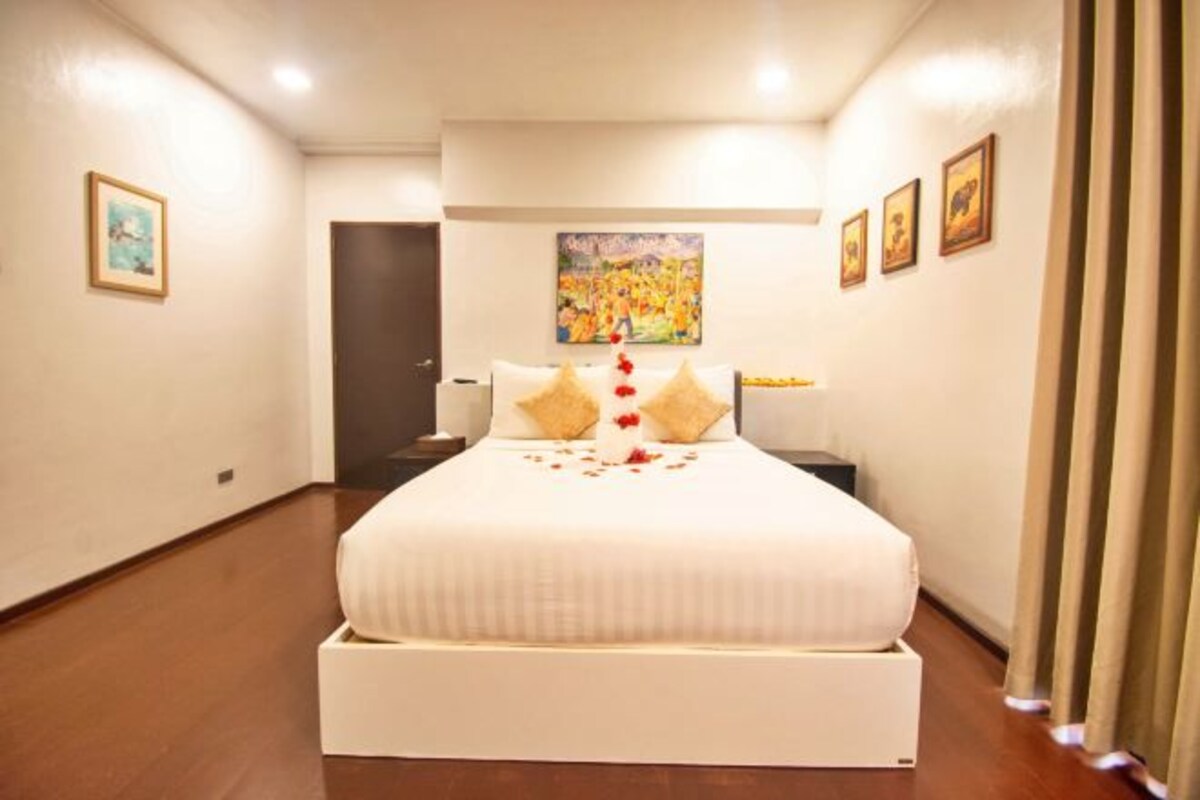 A hotel room with a large bed, a painting on the wall, and a door leading to another room.