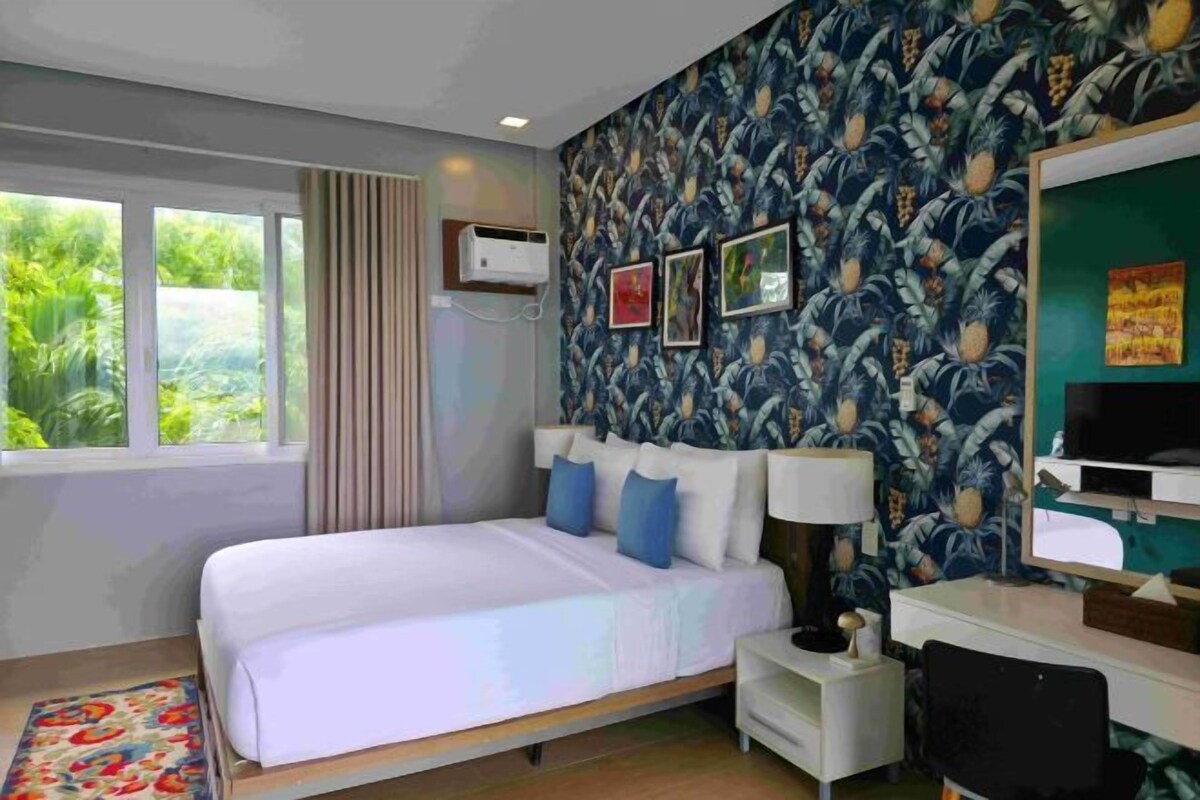 A hotel room with a bed, a desk, a chair, a TV, and a window with curtains.