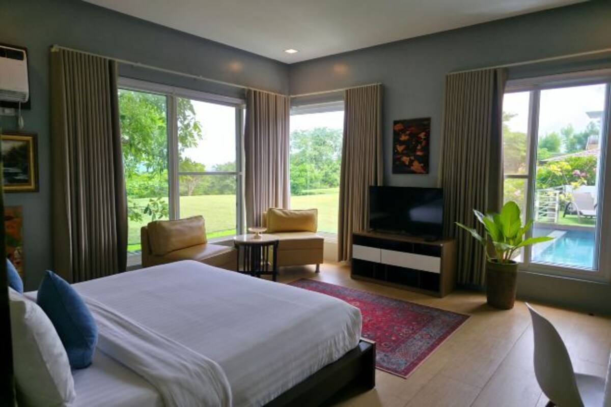 A spacious bedroom with a large bed, a TV, and a view of a swimming pool.