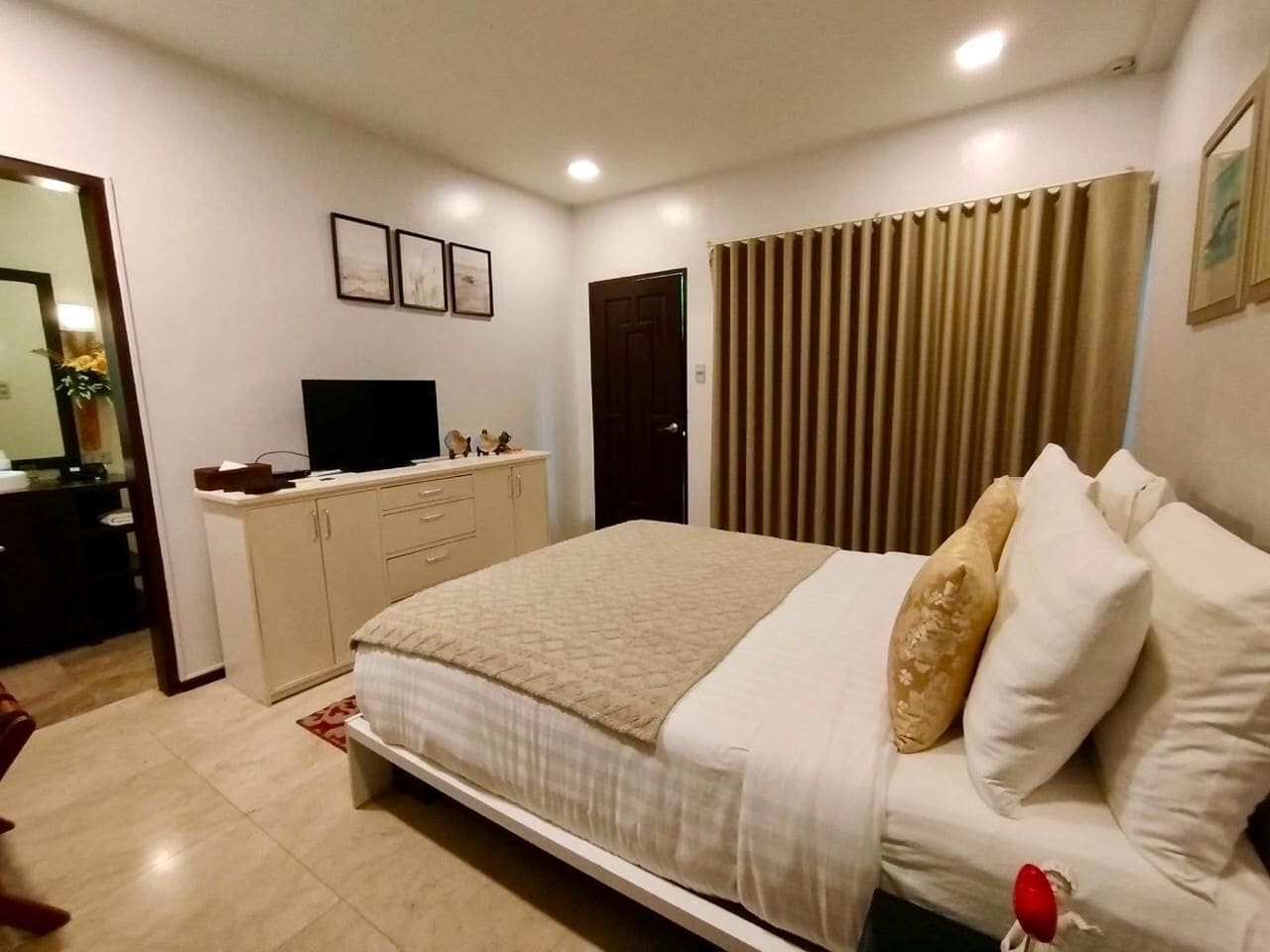 A bedroom with a bed, a dresser, a television, and a window with curtains.