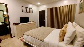 A bedroom with a bed, a dresser, a television, and a window with curtains.