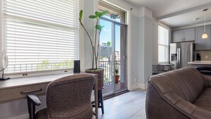 A modern kitchen with a refrigerator, a dining table, and a bar stool. There is a large window with blinds, a potted plant, and a view of the city. - Executive-next to Convention Center + Free Parking (Long Beach)