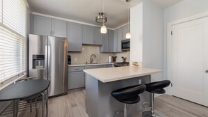 A modern kitchen with grey cabinets, a stainless steel refrigerator, a double sink, and a bar area with stools. - Executive-next to Convention Center + Free Parking (Long Beach)