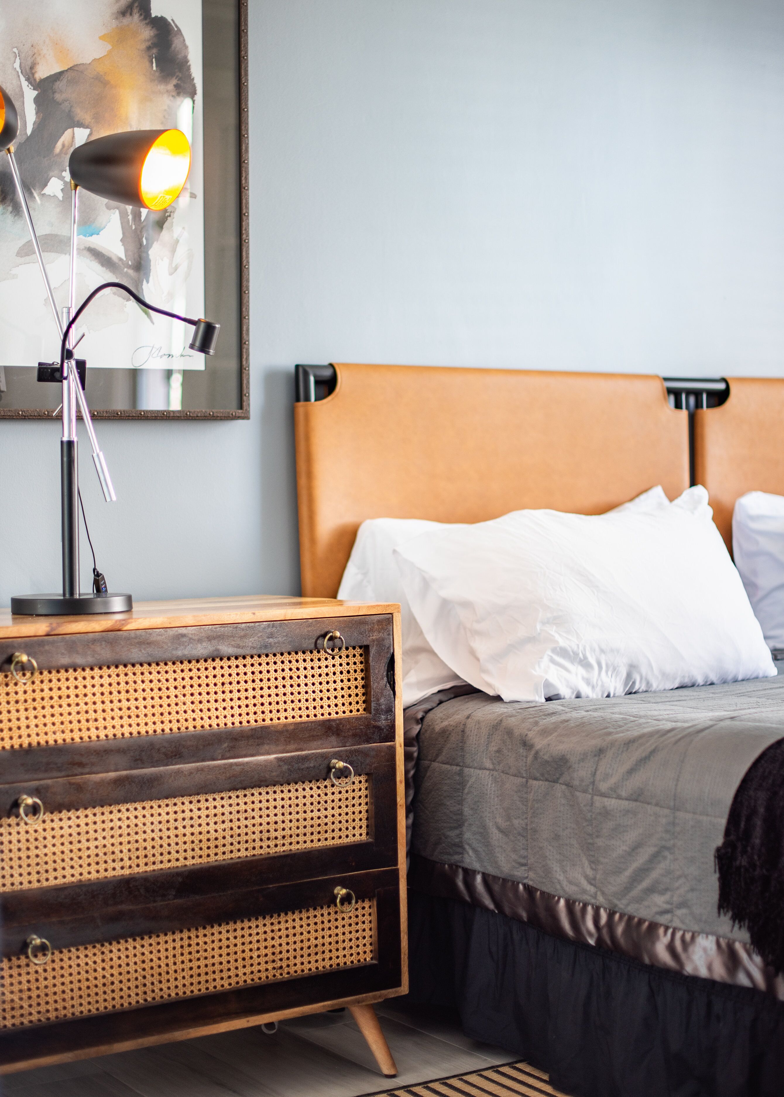 Une chambre à coucher avec une table de chevet en bois, un miroir, un lit avec une tête de lit et une table de chevet avec une lampe.