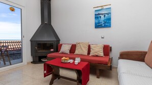 A cozy living room with a fireplace, a red sofa, a white sofa, and a table with a red tablecloth. - Mar i Muntanya II by Interhome (Llançà)
