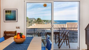 A dining area with a view of the sea, a wooden table with a fruit bowl, and a painting on the wall. - Mar i Muntanya II by Interhome (Llançà)