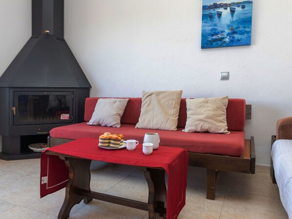 A cozy living room with a red sofa, a small table with snacks, a white mug, and a black fireplace.