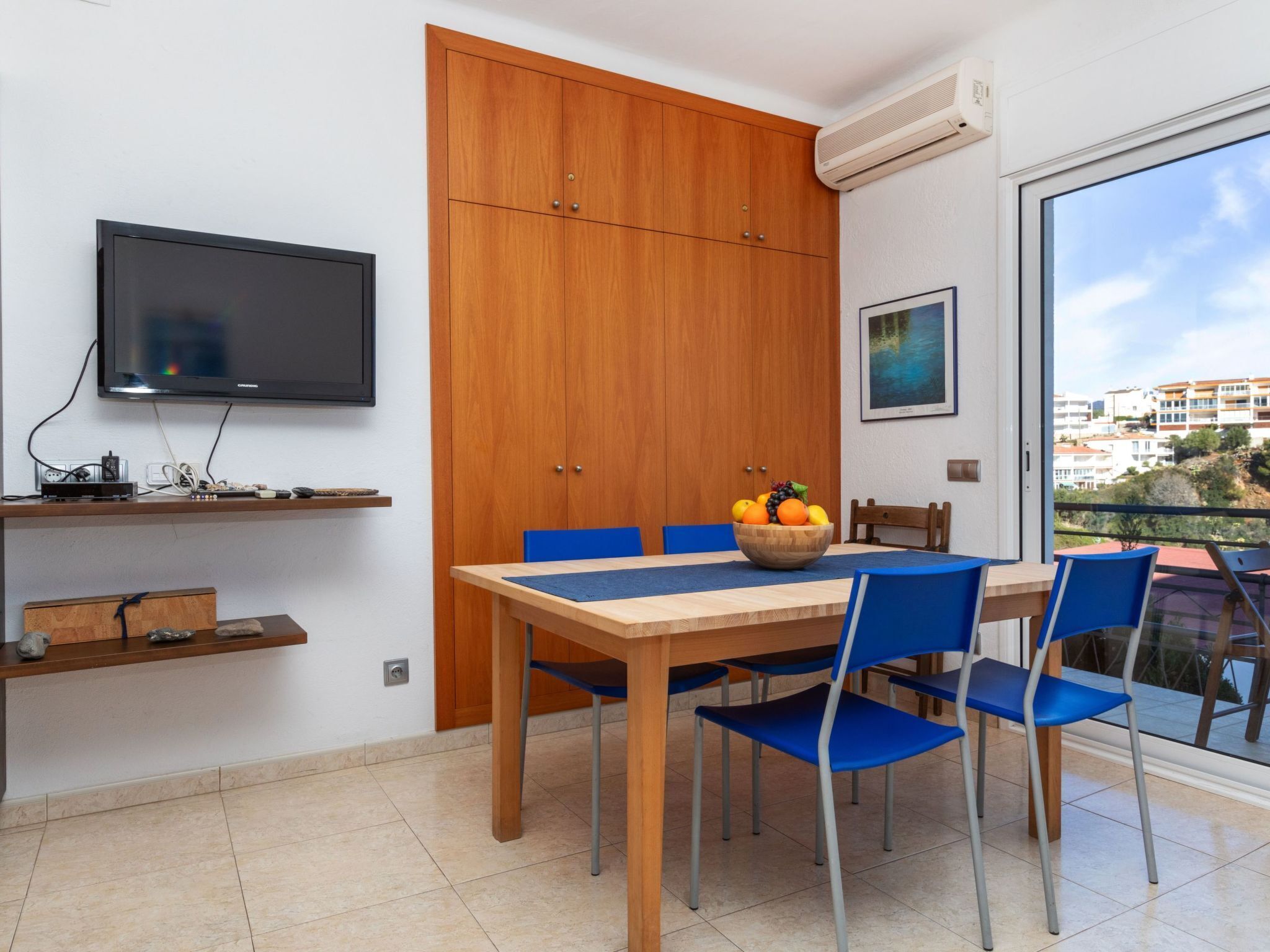 A modern dining area with a wooden table, blue chairs, and a fruit bowl.
