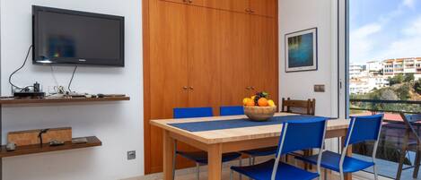 A modern dining area with a wooden table, blue chairs, and a fruit bowl.